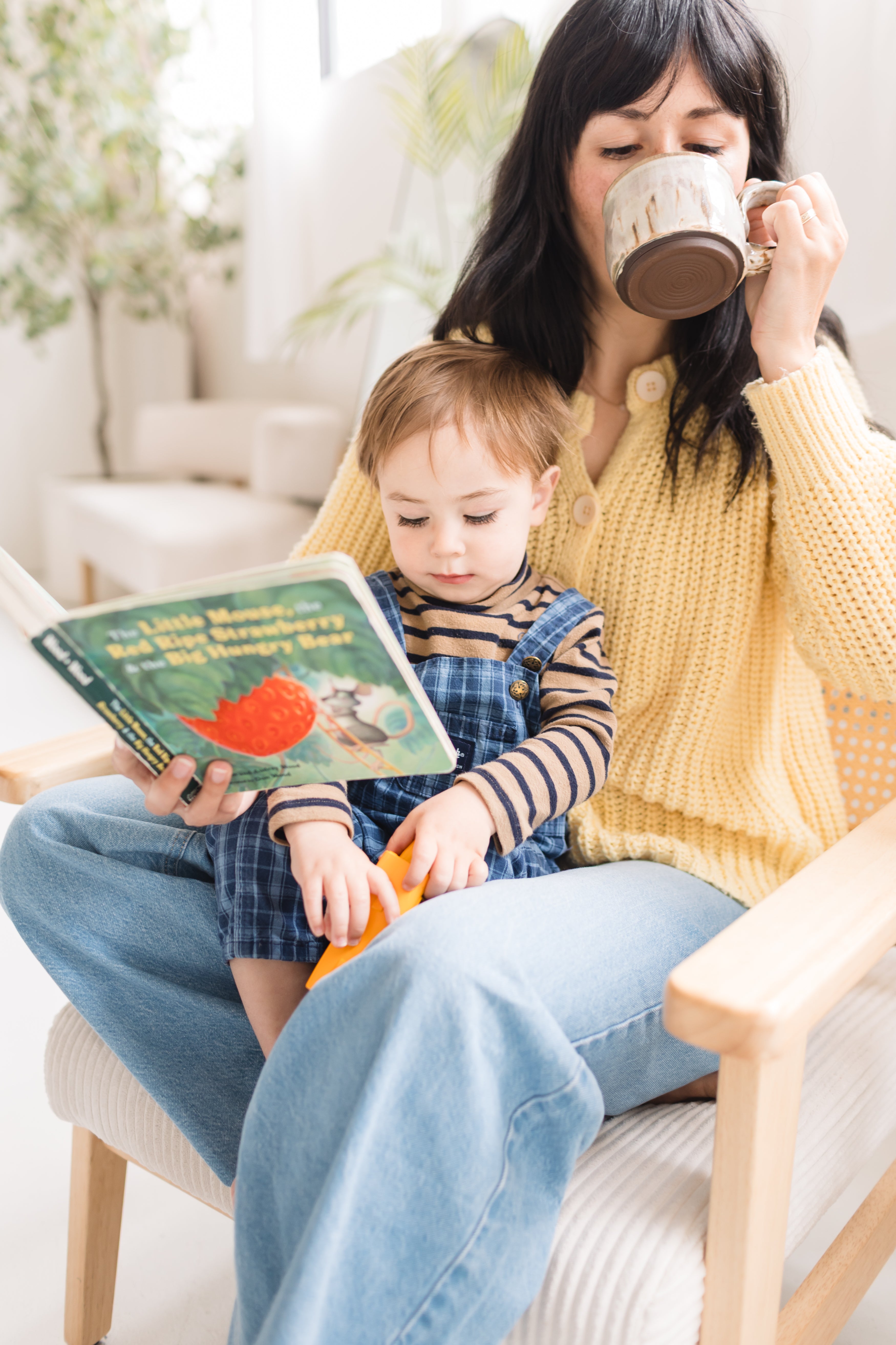 Woman and child sitting together, reading a book and drinking from mugs.