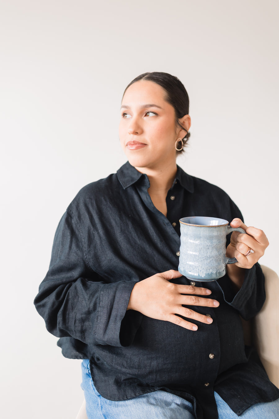 Pregnant woman holding a ceramic mug against a plain background