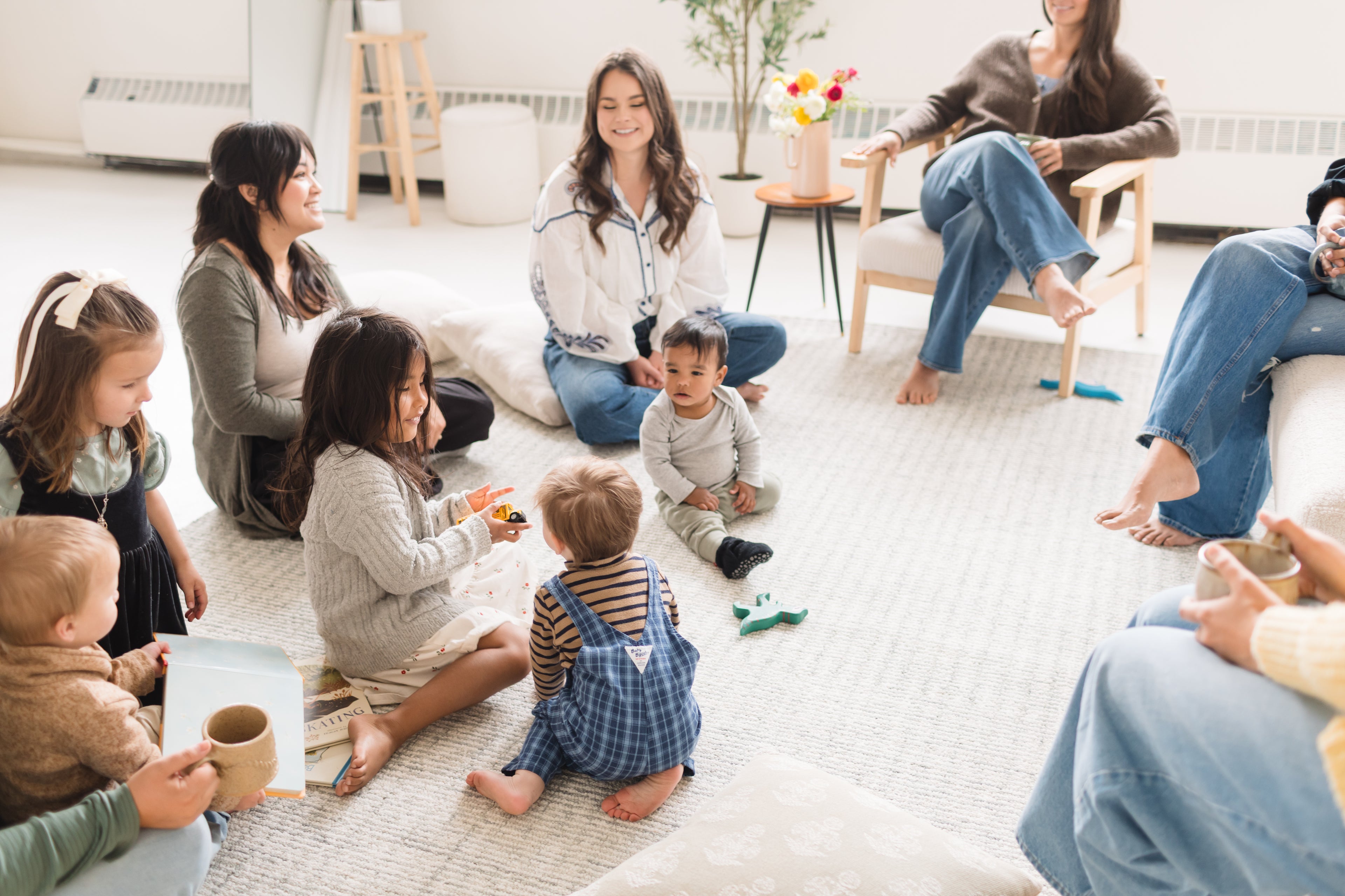 Group of women and children sitting on the floor in a circle, possibly in a community center or similar setting.